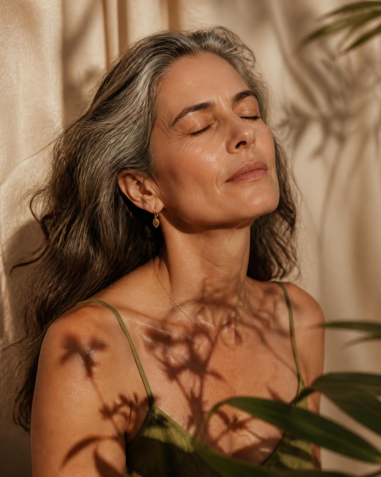 Mulher madura de olhos fechados, banhada por luz dourada e sombras de folhagem